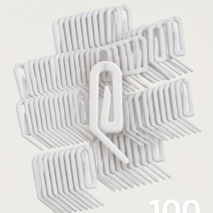 Fotografia de produto para e-commerce exibindo um conjunto de ganchos deslizantes brancos em plástico para trilho suíço de cortina. Um gancho individual aparece em destaque no centro, cercado por dezenas de unidades organizadas em pilhas sobre um fundo off-white limpo, com iluminação de estúdio suave. No canto inferior direito, há o texto discreto "100 UNIDADES" em tipografia branca legível.